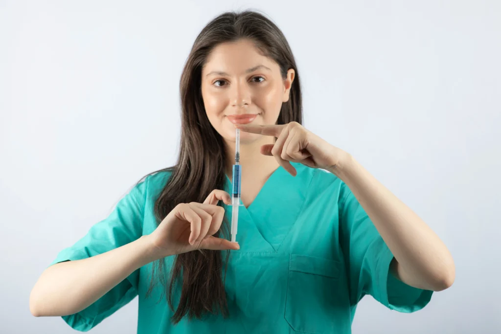 Healthcare worker in teal scrubs drawing liquid into a syringe to prepare an injection.